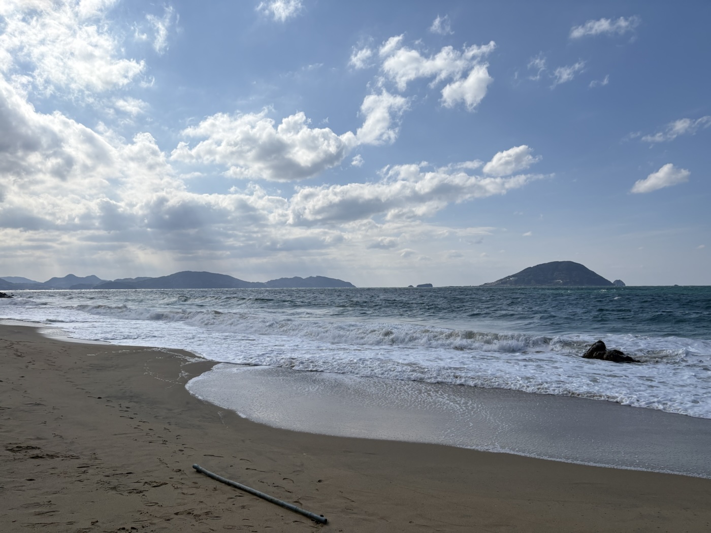 志賀島の砂浜に寄せる白い波と沖の島影